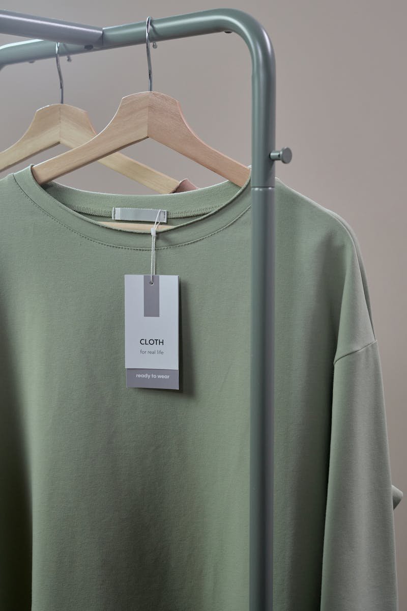 Close-up of a green shirt on a hanger with label tag on a minimalist clothing rack.