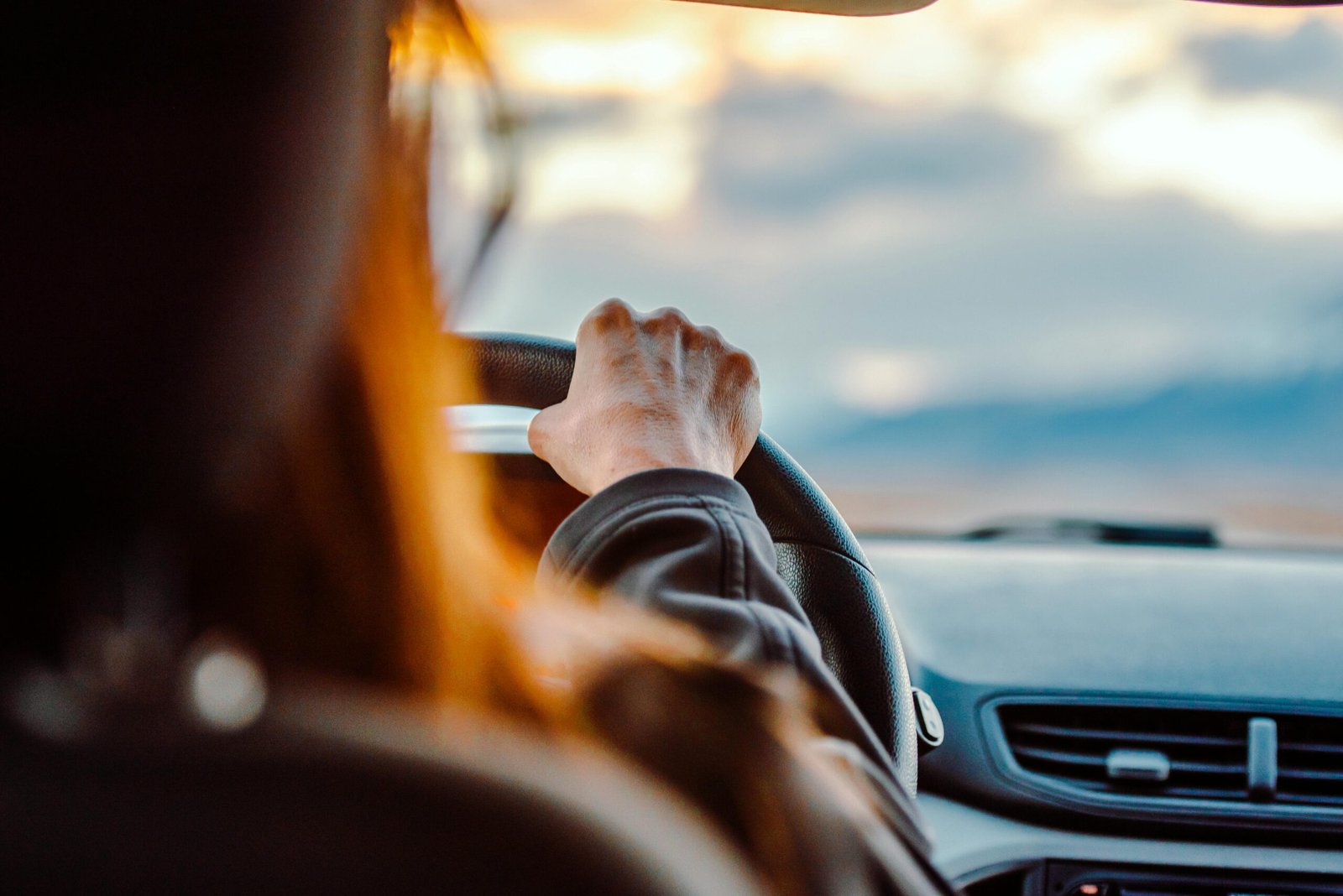 Close-up of a woman's hand on the steering wheel while driving with a scenic view ahead.