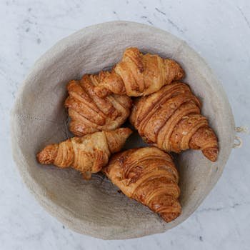 Top view of golden croissants in a linen basket, perfect for breakfast setting.