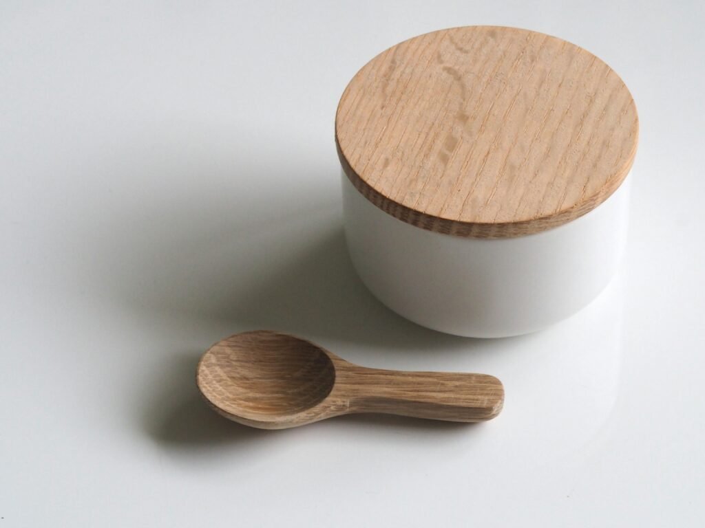 A white round container with a wooden lid and wooden spoon on a white surface. Simple and clean design.